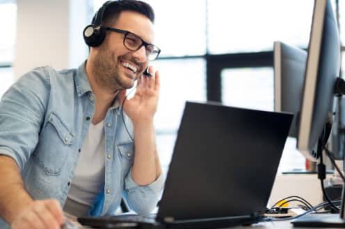 Managed IT Support Image - Man wearing a headset, smiling, looking at a laptop. 